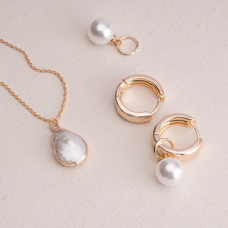Detail of stylish gold hoop earrings featuring removable pearl drops and necklace