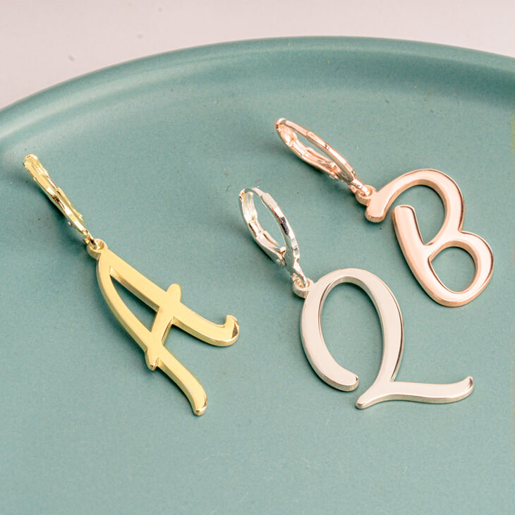 Cursive initial earrings showcased on a green plate, featuring trendy letter designs