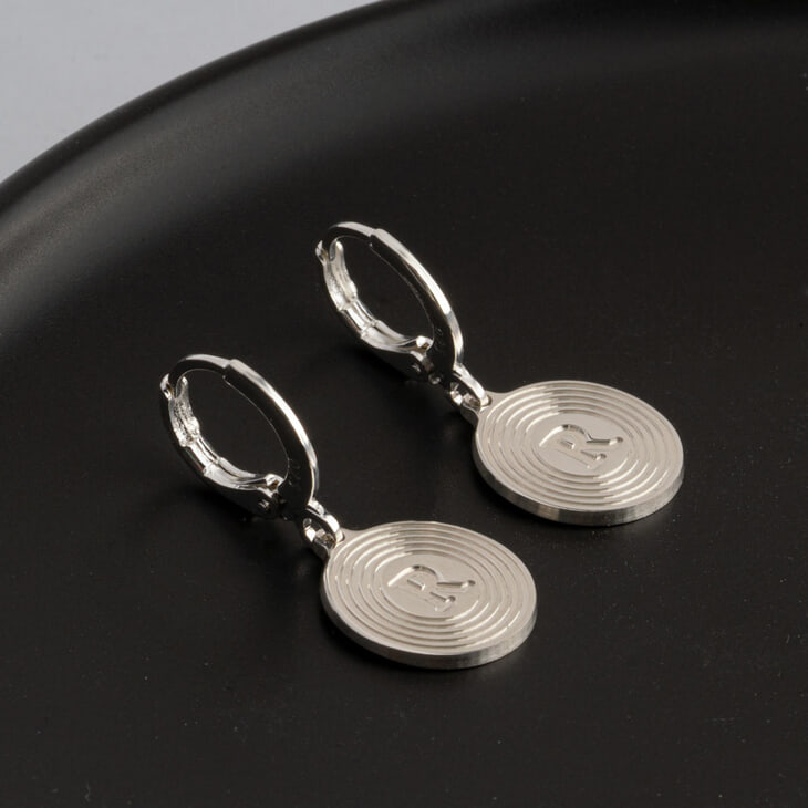 Stylish circle earrings showcasing initial R arranged on a dark plate
