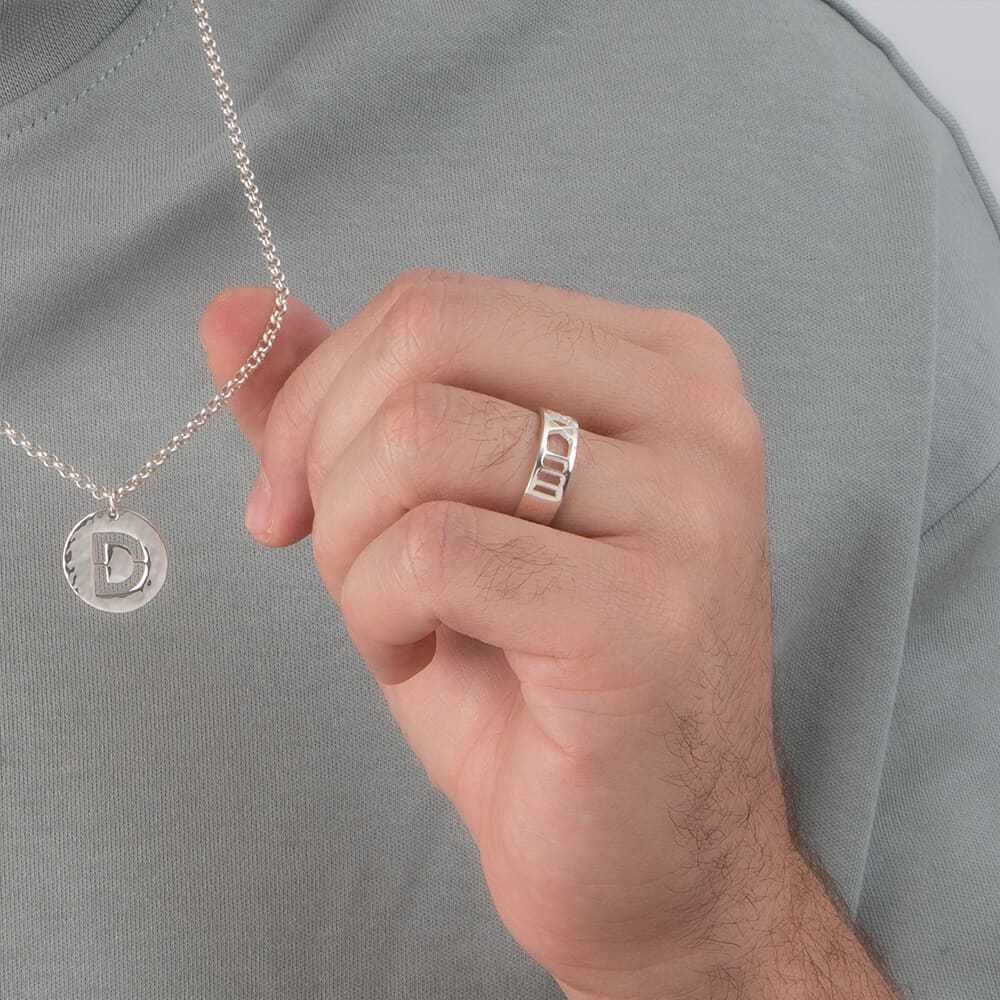 Casually dressed man showing a Custom Men's Roman Numeral Ring with a pendant necklace.