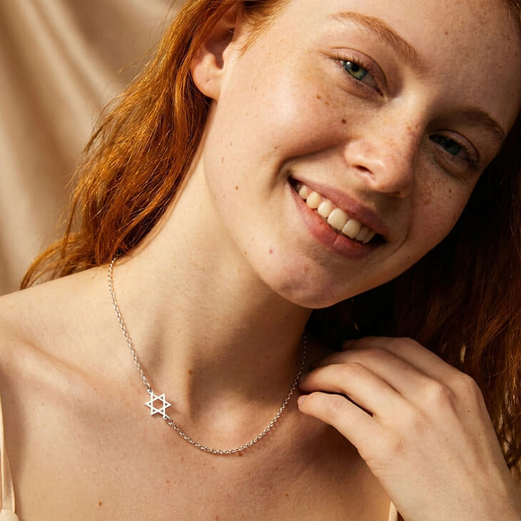 Woman displaying the Sideways Star of David Necklace with a cheerful pose, reflecting modern sophistication.