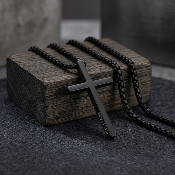 Men's Black Cross Necklace laid on a wooden block with unique engraving