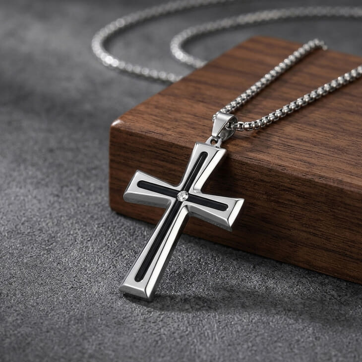 Men's Black Inlay Cross Necklace in silver laying on a wood surface