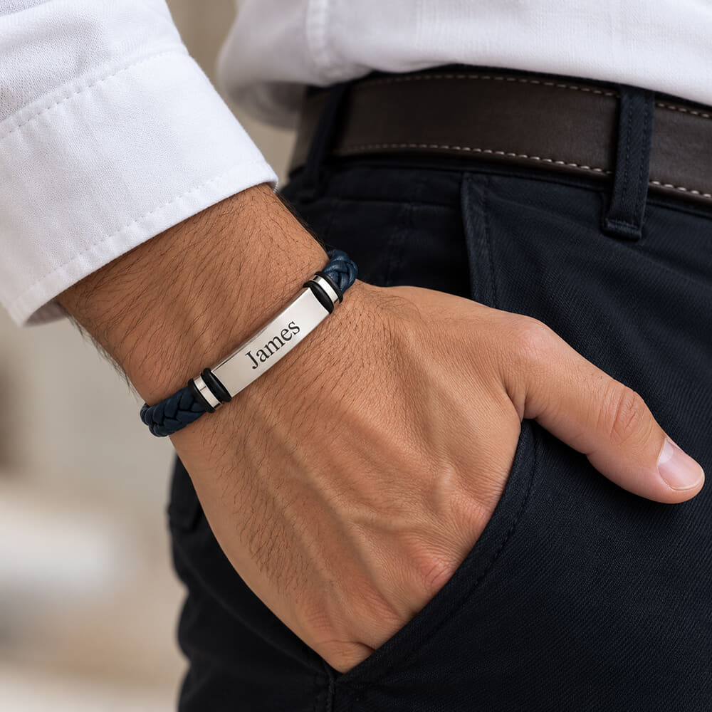 Person styling a navy blue braided leather bracelet with a custom engraved detail